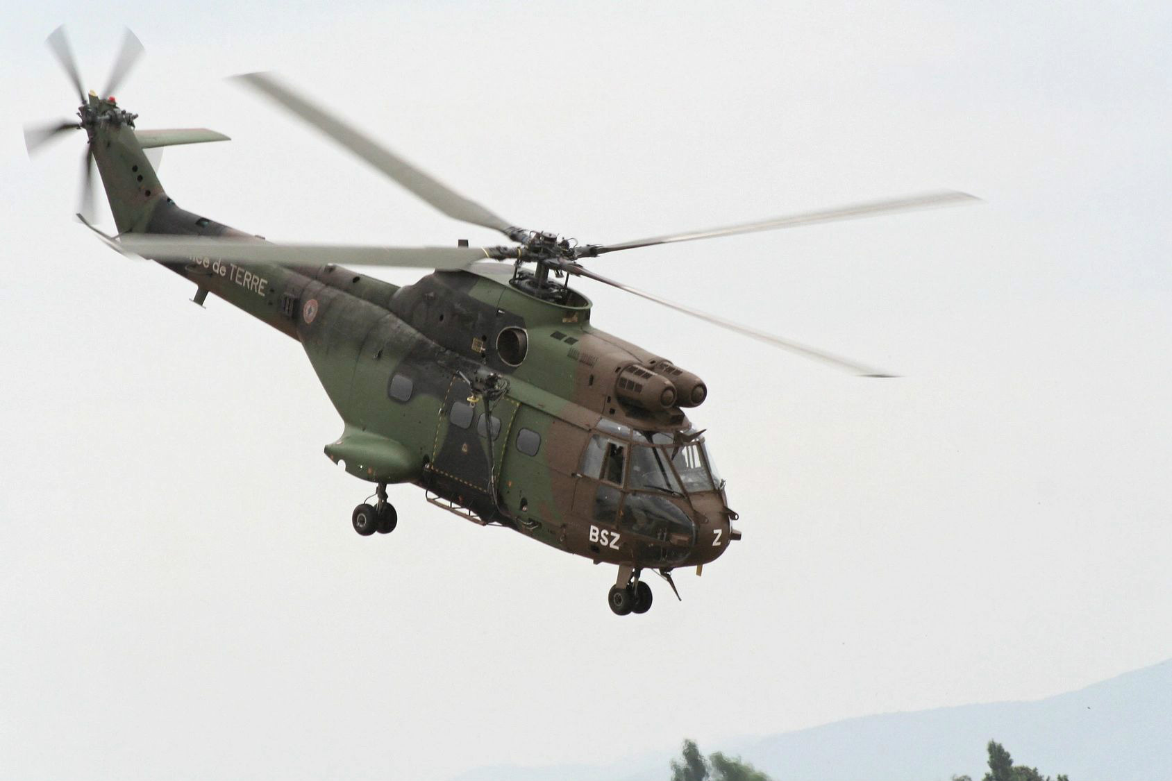 A helicopter flying in the sky with its landing gear down.