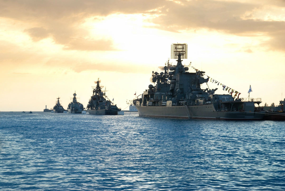A group of ships in the ocean at sunset.